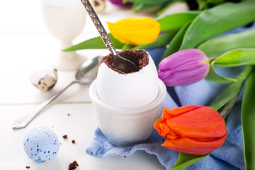 Easter egg filled with chocolate cake, tulips and colorful quail eggs on white background. Easter holidays breakfast concept.