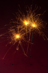 Three sparklers burning against a dark red background, party concept