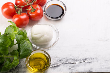 Ingredients for cooking italian capreze salad cherry tomatoes, basil leaves, mozzarella cheese, spices and olive oil on wooden rustic background top view close up
