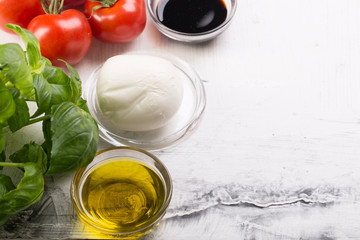 Ingredients for cooking italian capreze salad cherry tomatoes, basil leaves, mozzarella cheese, spices and olive oil on wooden rustic background top view close up