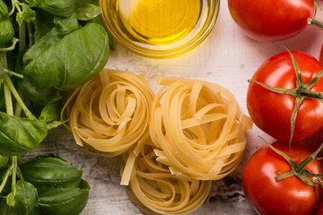 Italian food background with vine tomatoes, basil, tagliatelle pasta on white background Top view