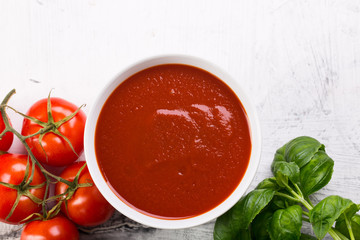 Tomato soup with basilic, cherry tomatoes on white background Top view