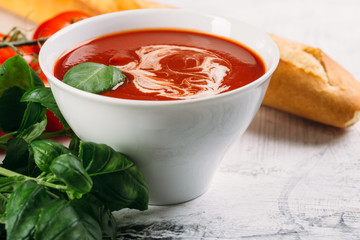 Tomato soup with basilic, cherry tomatoes and baguette on white background Top view