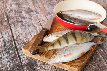 River fish.   Fresh river fish, perch and roach, on a cutting board and in a frying pan on an old...