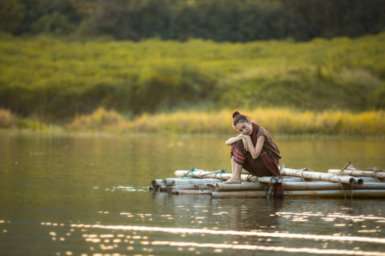 girl style alone, sitting on a bamboo raft in a river with lonel