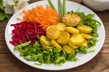 Dish with fried potatoes, beets, carrots and lettuce on a background of flowers. Wooden table. Close-up