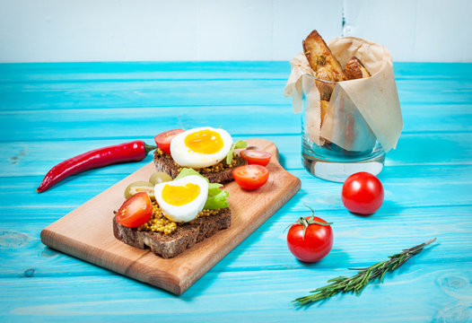 Sandwiches with olive, quail eggs, cherry tomatoes and potatoes on a wooden blueboard.