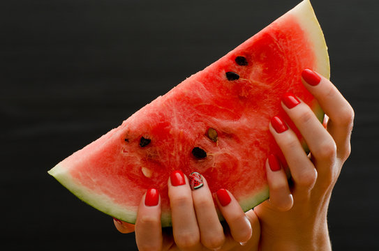 Large slice of ripe watermelon in female hands on a black background, close-up