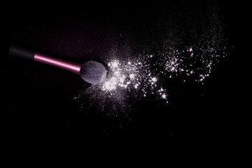 Make-up brush with colorful powder spilled glitter dust on black background. Makeup brush on new year's Party with bright colors. White powder on black table.
