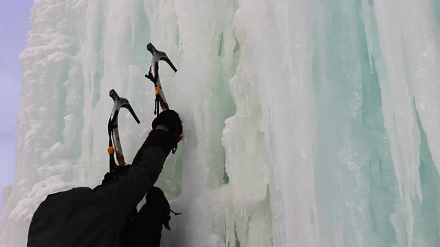 Young man with ice axes and crampons training to climb on icefall
