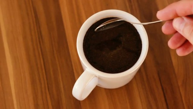 Male hand stirring a cup of coffee standing on wooden table. Top view. Slow motion