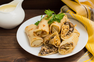 Pancakes stuffed with mushrooms and sour cream on a rustic wooden table. Top view. Close-up