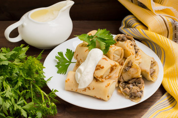 Pancakes stuffed with mushrooms and sour cream on a rustic wooden table. Top view. Close-up