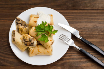Pancakes stuffed with mushrooms and sour cream on a rustic wooden table. Top view. Close-up