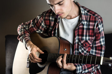 Young man playing chord on guitar. Male musician in casual wear plays acoustic instrument and holds...