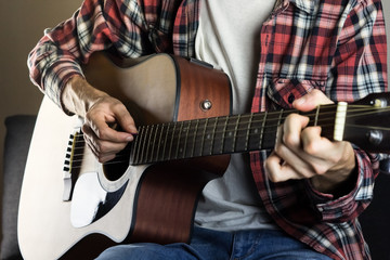 Playing instrument at home. Male hands playing chord on acoustic guitar