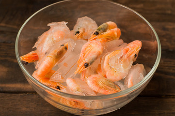 Frozen raw shrimp in a transparent plate of ice. Wooden background. Top view. Close-up