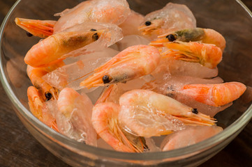 Frozen raw shrimp in a transparent plate of ice. Wooden background. Top view. Close-up