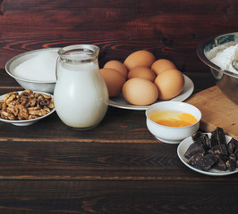 Baking ingredients: milk, sugar, eggs, chocolate, walnuts on rustic wood
