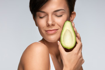 Skin Care And Beauty. Beautiful Woman Holding Avocado Near Face