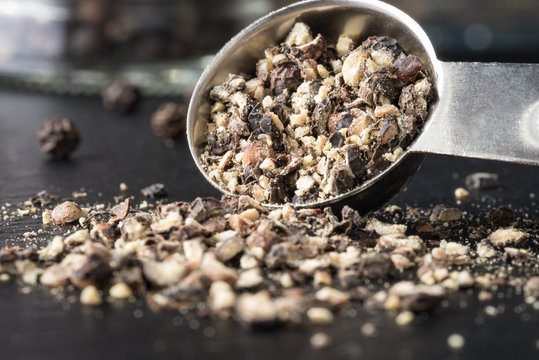 Coarsely ground black pepper spilling from a measuring spoon