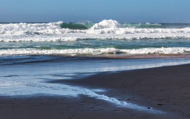 Adraga Beach (Praia da Adraga) in Portugal. Beautiful place, golden sand. Rough sea, rocks, whitewash, blue sky.