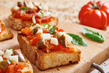 Fototapeta na wymiar Bruschetta tomato, cheese, olives and garlic on cutting board and wooden table