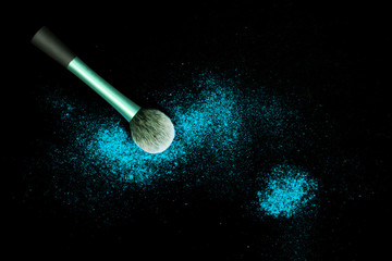Make-up brush with colorful powder spilled glitter dust on black background. Makeup brush with bright colors. Turquoise powder on black table.