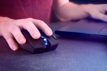 Man holding gaming mouse and laptop screen glowing at night.