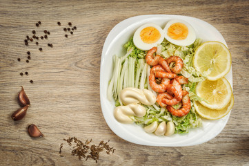 shrimp on a salad with sauce, lemon, egg, garlic cloves in a bowl on a wooden background. Close-up