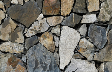 Stone wall consisting of various different colored stones in a mosaic like pattern. The shapes of the stone blocks are irregular but fitting precisely with only small gaps.