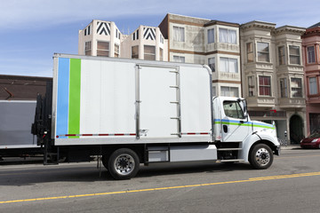 Delivery truck on city street with buildings and blue sky in background. Horizontal.