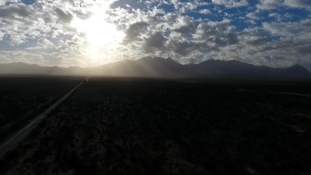 Aerial shot of a desolate road heading towards mountains and sun rays