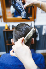 man getting groomed by hairdresser with hair dryer at barbershop