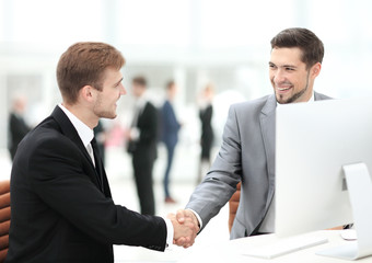 Two happy young men shaking hands while sitting at the office