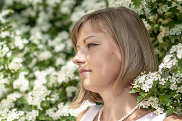 Young blonde woman in a white dress walks in the spring park
