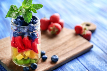 Glass jar with fruits and berries on wooden background