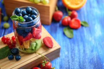 Glass jar with fruits and berries on wooden box