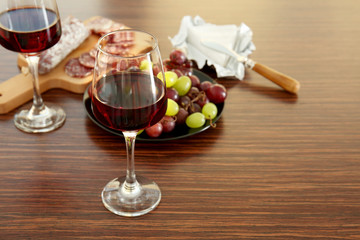 Glasses with red wine, grape, wurst and cheese on wooden background