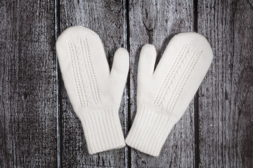 Knitted woolen white mittens on a rustic wooden background
