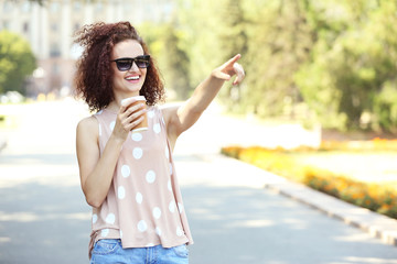 Young cheerful woman with cup of coffee walking in the park