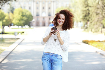 Young cheerful woman with cup of coffee walking on the street