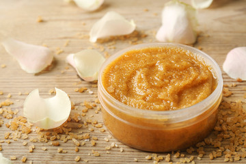 Body scrub, petals and sugar on wooden background