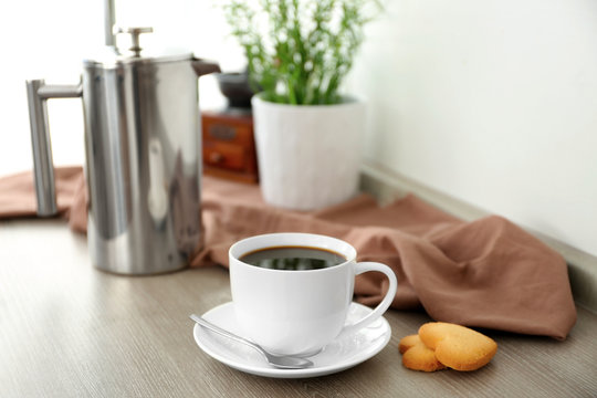 Cup of coffee with cookies and coffee pot on kitchen table