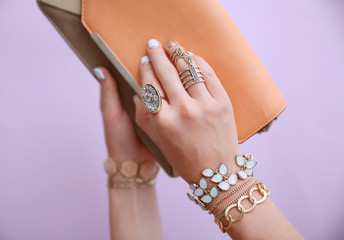 Female hands with jewelry and clutch bag on color background