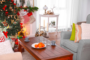 Wooden table with candles, cups and oranges in living room decorated for Christmas