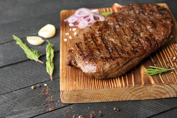 Delicious steak with aromatic rosemary and onion on board and grey wooden background