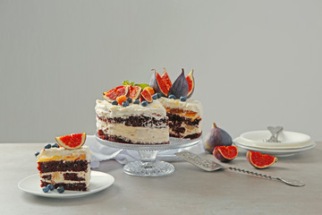 Delicious creamy cake with figs and berries on light grey background