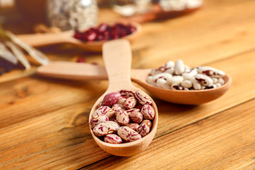 Assortment of haricot beans in spoons on wooden background