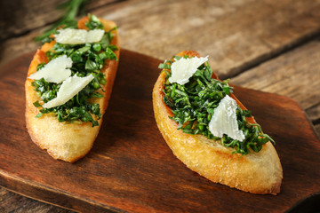 Delicious bruschetta with chopped greens and cheese slices on wooden board, closeup
